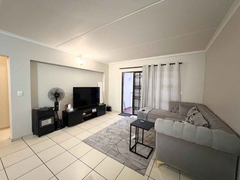 A well-lit living room featuring neutral tiled flooring, a recessed wall niche, and direct access to an outdoor area through a sliding door.