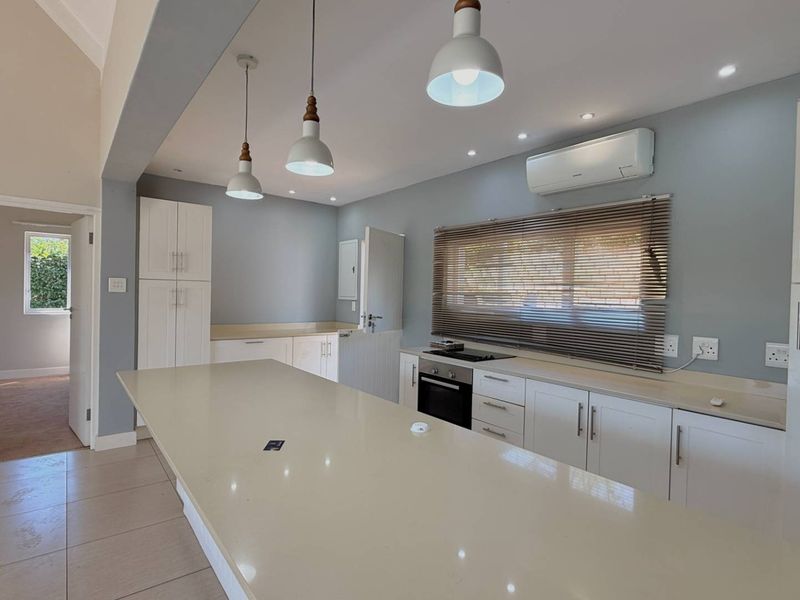 Modern kitchen featuring a large central island, quartz countertops, built-in oven, hob, and sleek white cabinetry with contemporary pendant lighting.