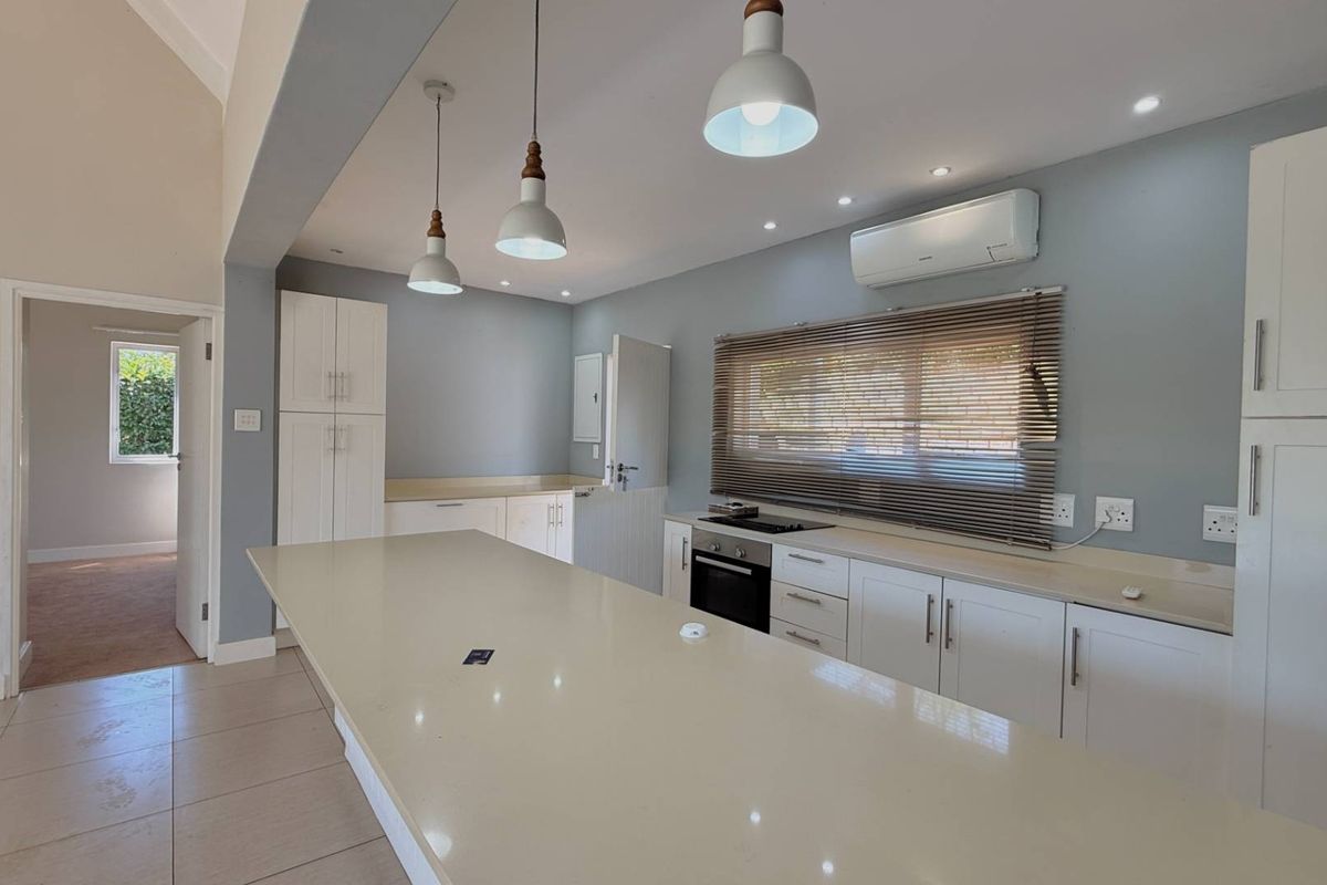 Modern kitchen featuring a large central island, quartz countertops, built-in oven, hob, and sleek white cabinetry with contemporary pendant lighting.