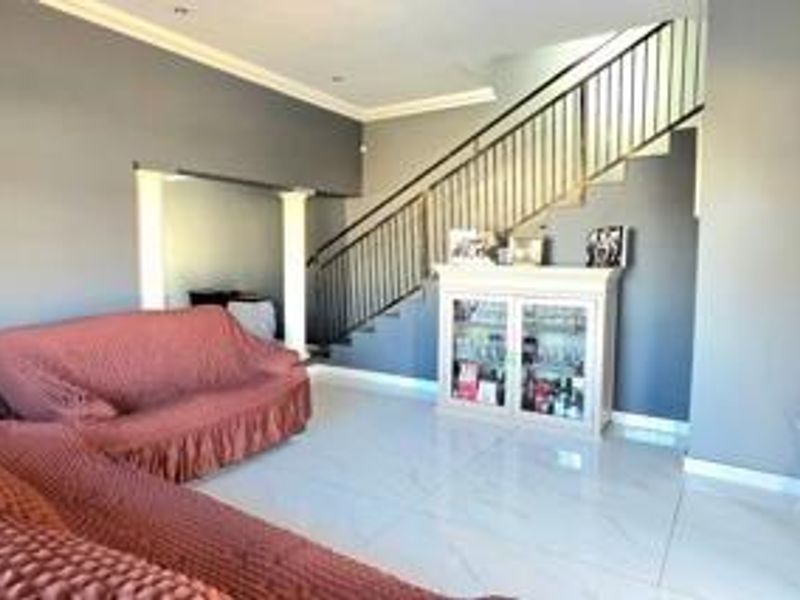 Spacious living area featuring polished tiled flooring, recessed lighting, and a prominent staircase with a modern metal balustrade.