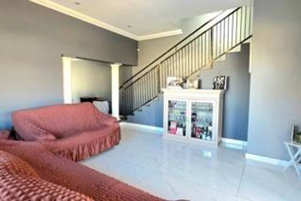 Spacious living area featuring polished tiled flooring, recessed lighting, and a prominent staircase with a modern metal balustrade.