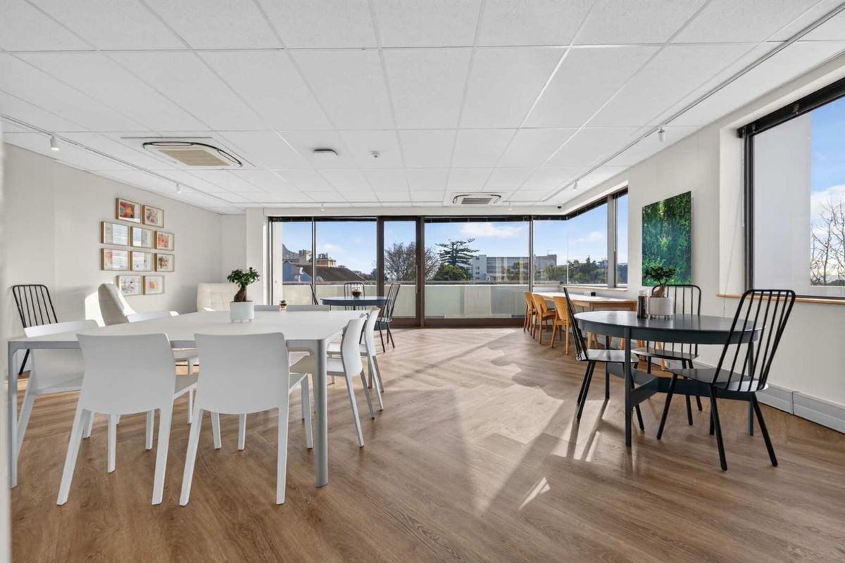 Bright and spacious open-plan office area featuring herringbone timber flooring, recessed ceiling lighting, and large windows providing ample natural light and exterior views.