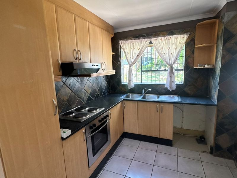 A functional kitchen featuring light wood cabinetry, a built-in oven and hob, tiled splashbacks, and a double sink with an open under-counter space.