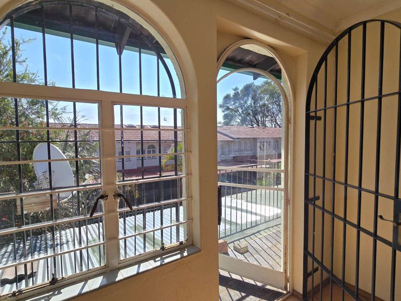 A covered balcony area featuring arched windows and a security gate, offering an outdoor transition space with views of the surrounding complex.