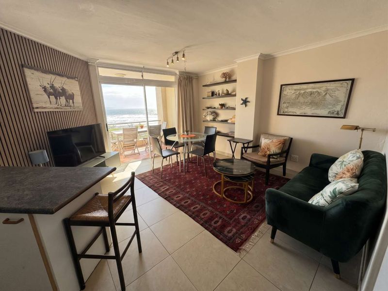 Open-plan living and dining area featuring tiled floors, built-in shelving, and a sliding glass door leading to a balcony with ocean views.