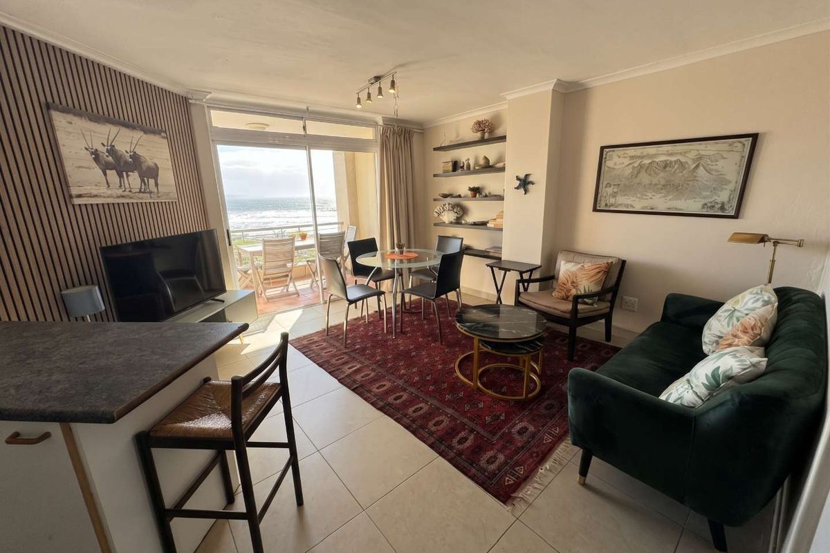 Open-plan living and dining area featuring tiled floors, built-in shelving, and a sliding glass door leading to a balcony with ocean views.