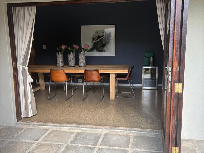 A covered patio with stone tile flooring leading through timber folding doors into a dining area with polished concrete floors and a dark accent wall.