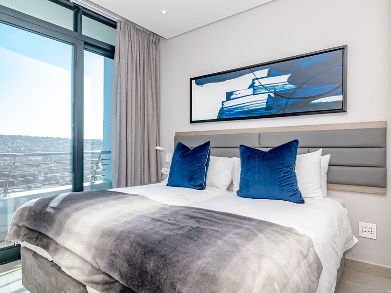 Modern bedroom featuring a large floor-to-ceiling sliding glass door with access to a balcony and integrated headboard lighting.