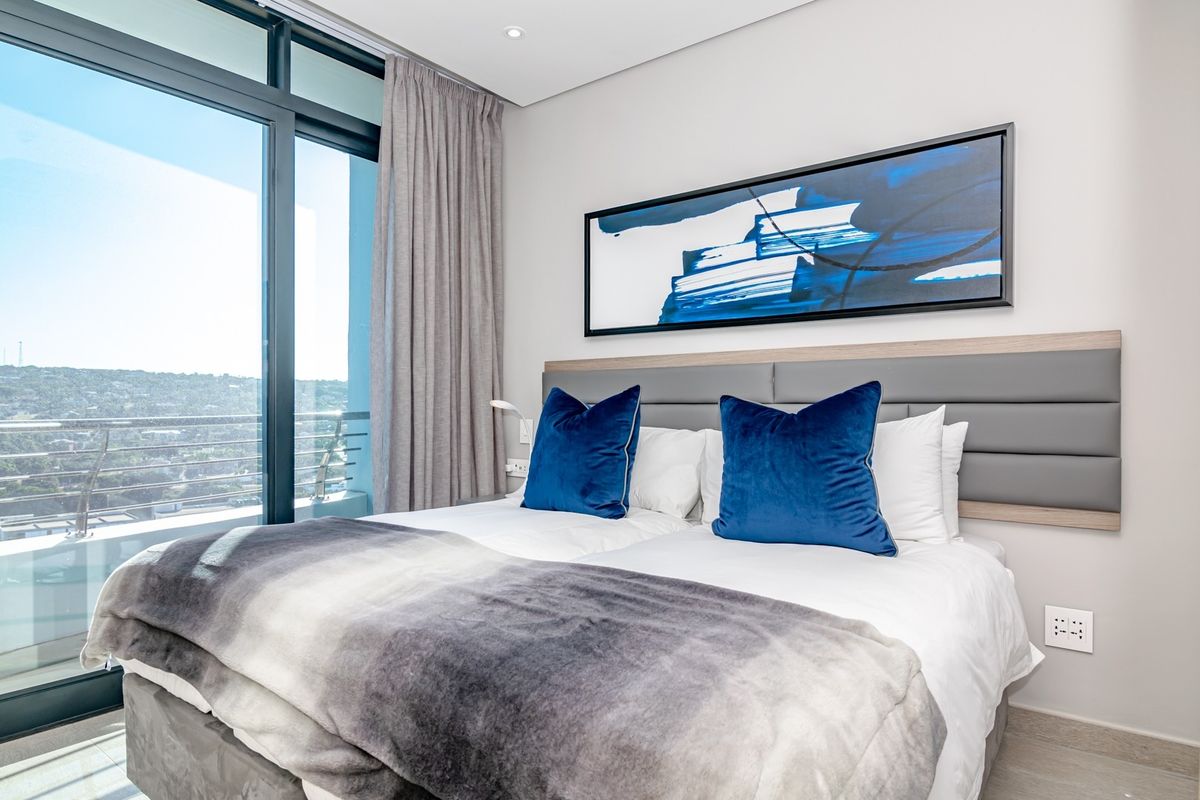 Modern bedroom featuring a large floor-to-ceiling sliding glass door with access to a balcony and integrated headboard lighting.