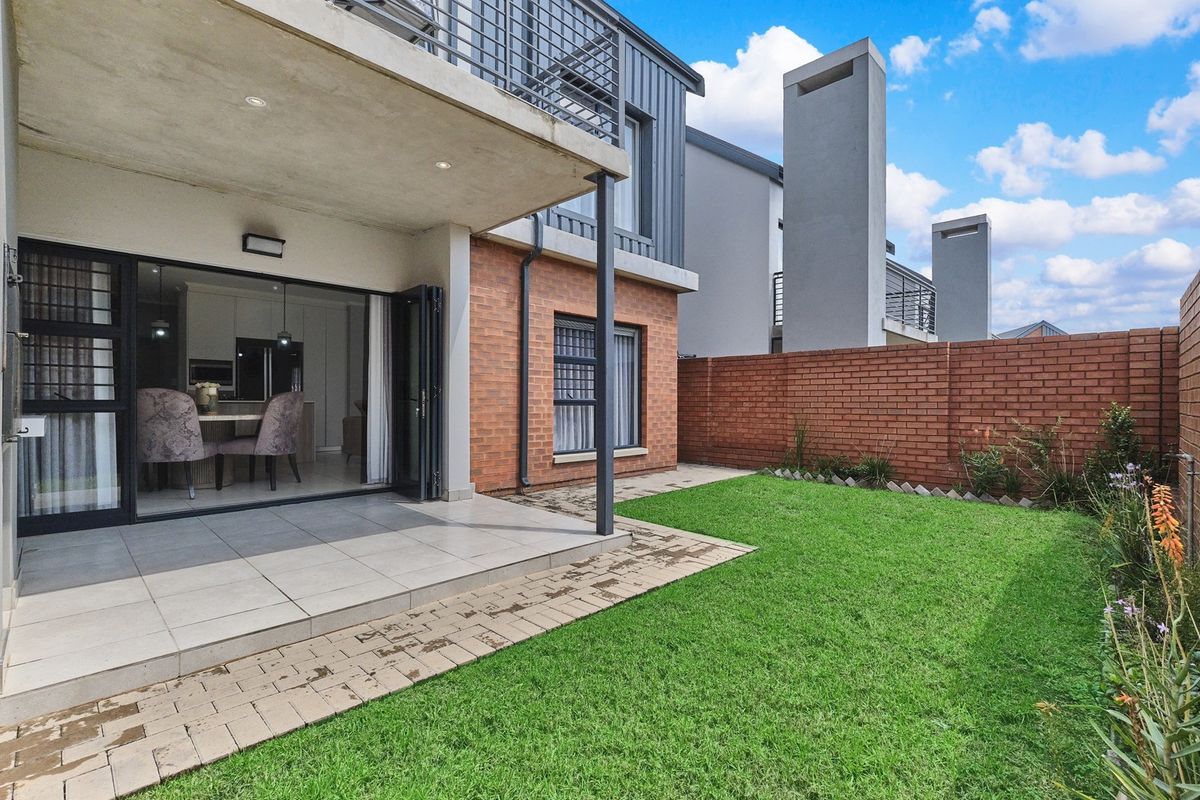 Rear view of the cluster property featuring a covered tiled patio, private garden with lawn, brick boundary wall, and access to the interior living area.