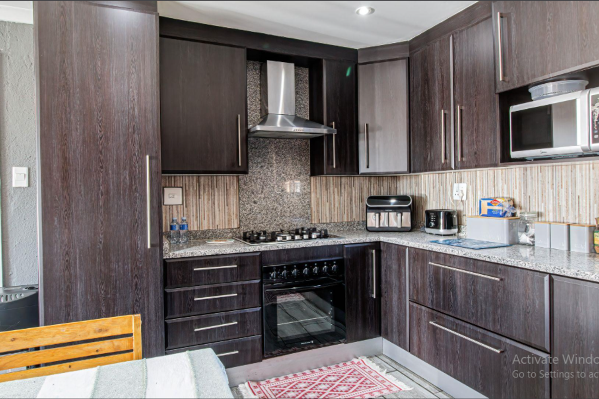 A modern kitchen featuring dark wood cabinetry, granite countertops, a gas hob, built-in oven, and stainless steel extractor fan.