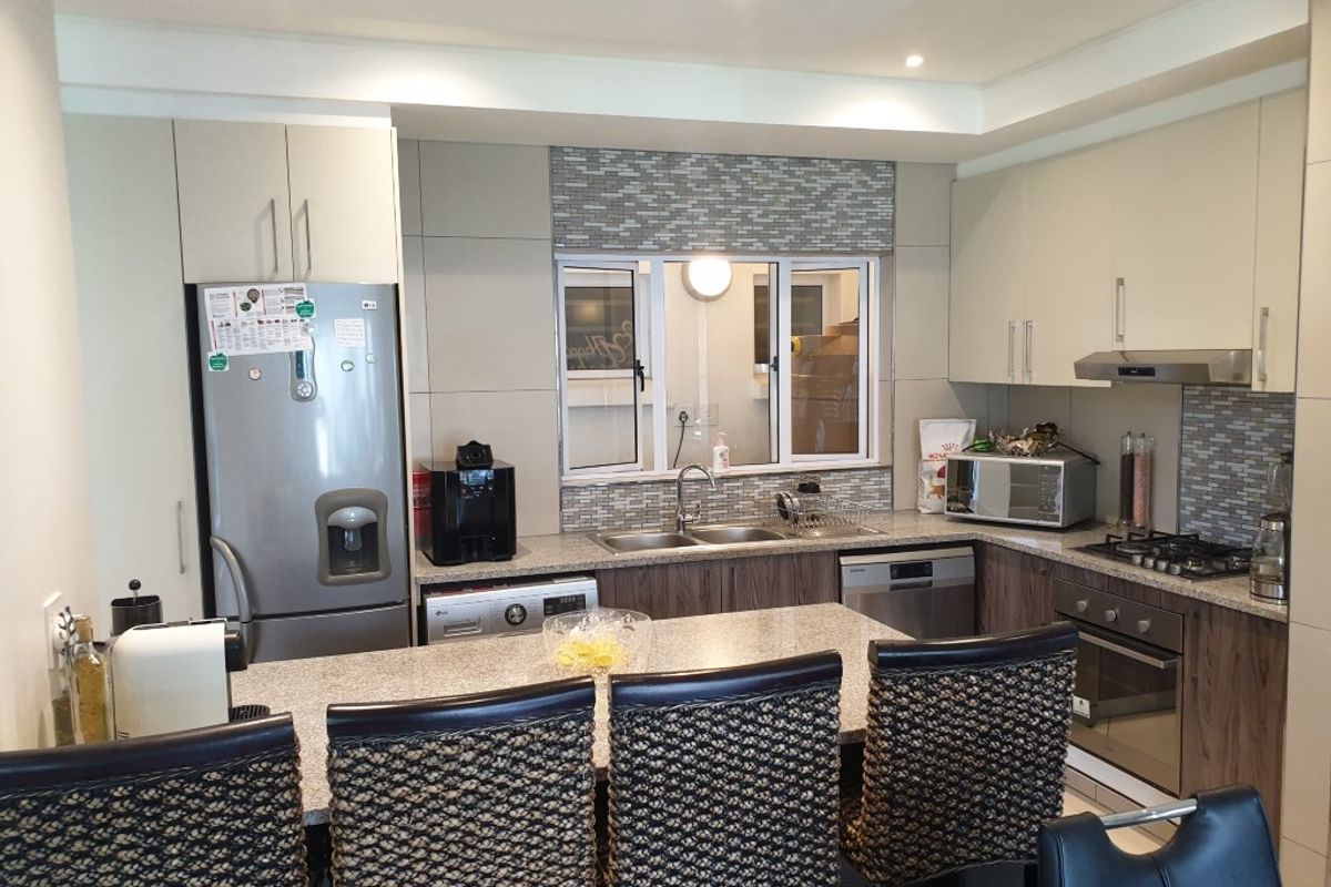 Modern kitchen featuring granite countertops, built-in oven, gas hob, extractor fan, and integrated cabinetry with a breakfast bar island.