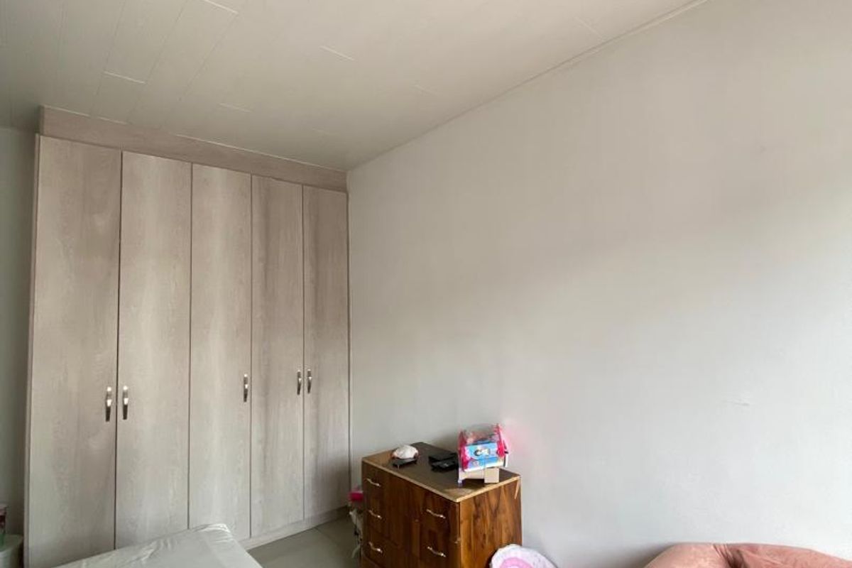 A bedroom featuring built-in light wood-grain wardrobes, tiled flooring, and a flush-mount ceiling light fixture.