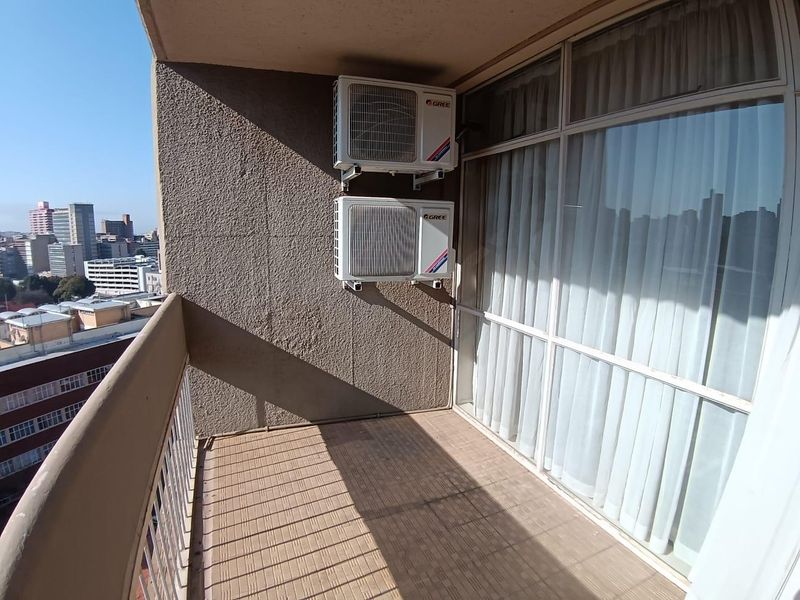 A functional apartment balcony featuring tiled flooring, a metal balustrade, and two wall-mounted air conditioning condenser units.