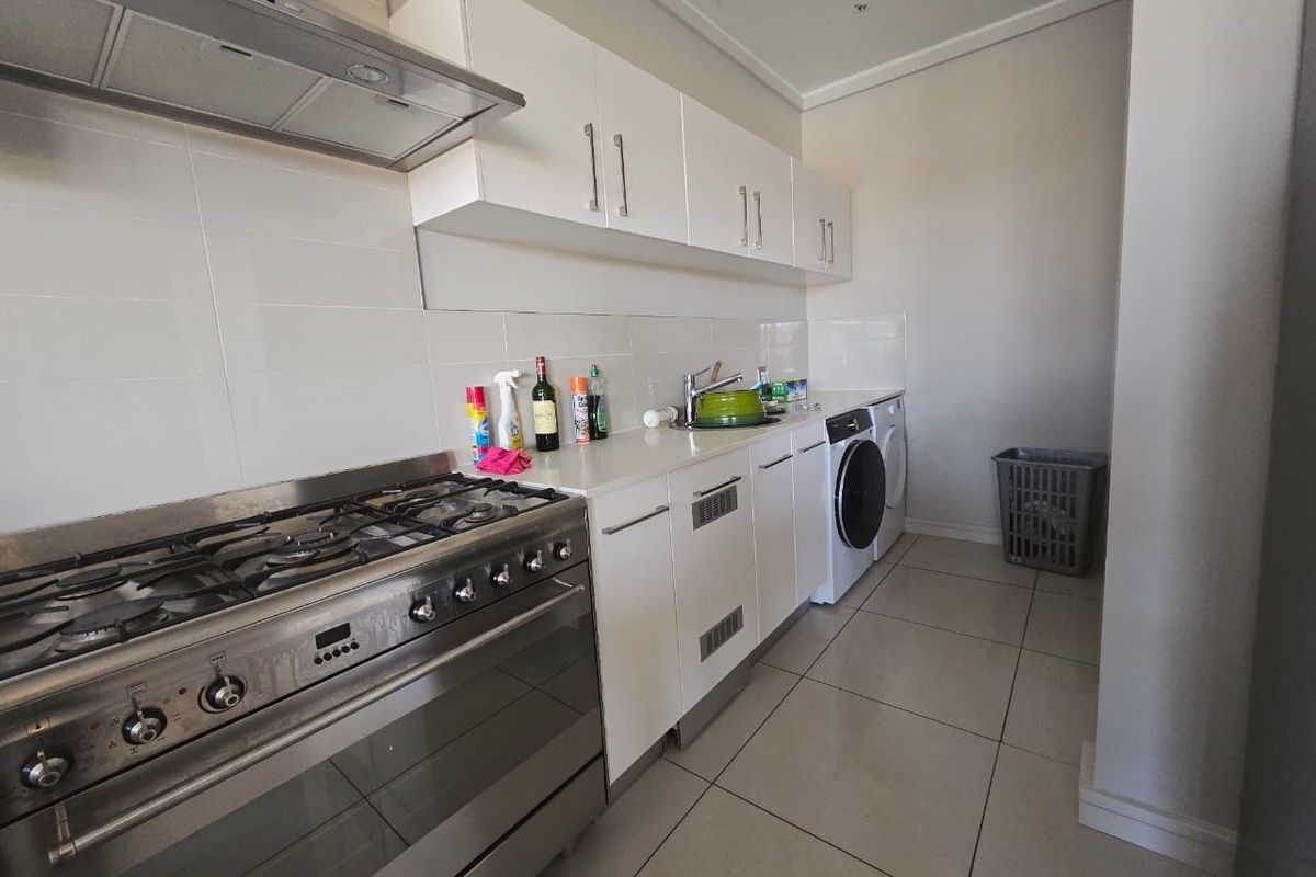 A functional kitchen featuring white cabinetry, a gas stove with extractor fan, tiled backsplash, and integrated space for laundry appliances.