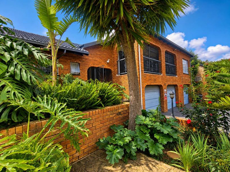 Front elevation of a double-story face brick house featuring a paved driveway, double garage, and established garden with mature trees.