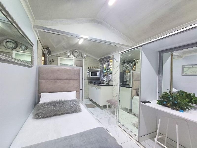 Compact open-plan studio space featuring a kitchenette, built-in wardrobe, vanity area, and tiled flooring under a vaulted ceiling.