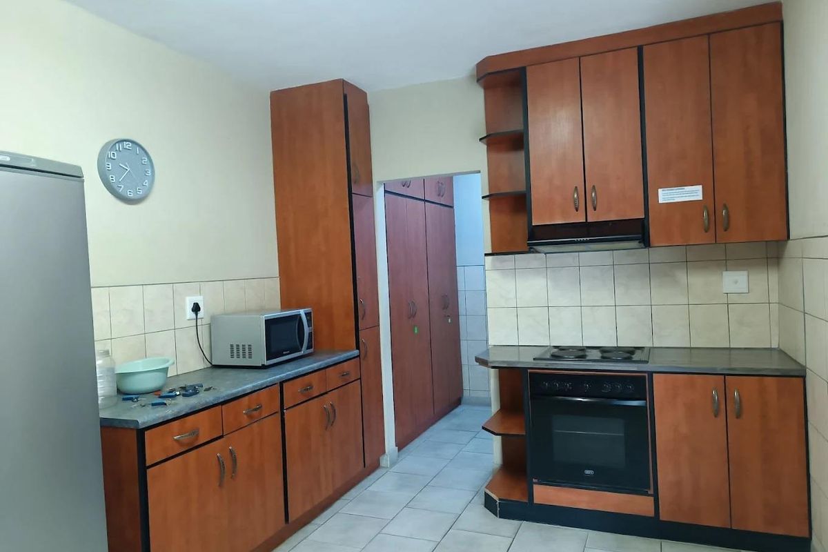 Functional kitchen featuring wood-finish cabinetry, built-in oven, electric hob, extractor fan, and tiled flooring with an adjacent scullery area.