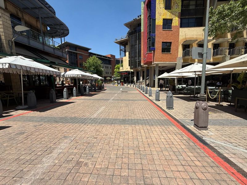 A view of a paved pedestrian street lined with multi-story commercial office buildings and outdoor seating areas.