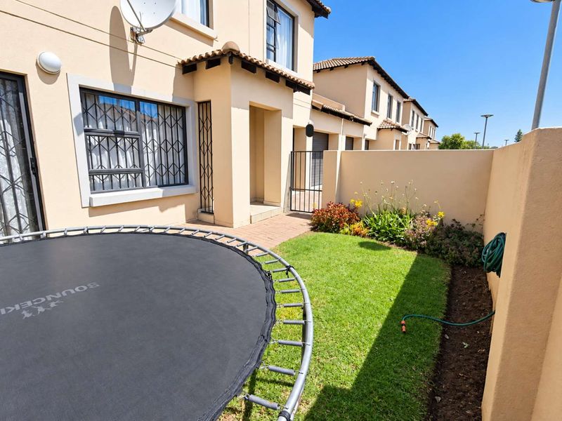 A private rear garden area featuring a small lawn, paved walkway, and boundary wall, attached to the townhouse structure with security bars on windows.