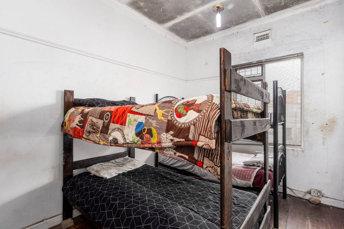A bedroom featuring timber flooring and a ceiling vent, currently showing significant signs of wear including wall staining and ceiling damage.
