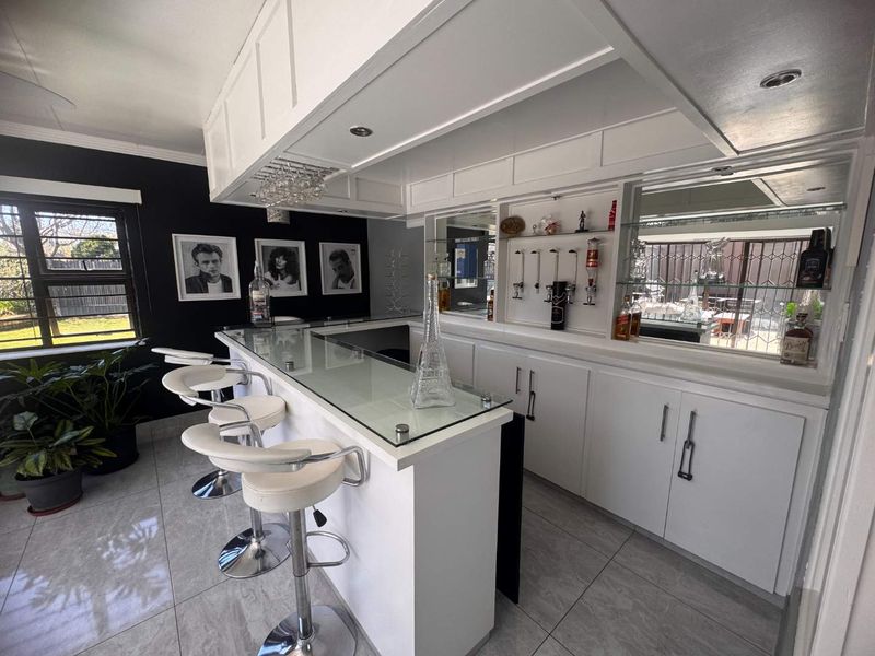 A well-appointed home bar featuring a glass-topped counter, custom white cabinetry, mirrored backsplash, and recessed lighting, creating a sophisticated space for entertaining.