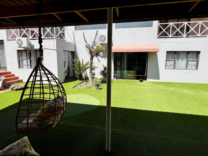 A private rear courtyard featuring a covered patio, artificial lawn, and access to the main dwelling via sliding doors and a balcony above.