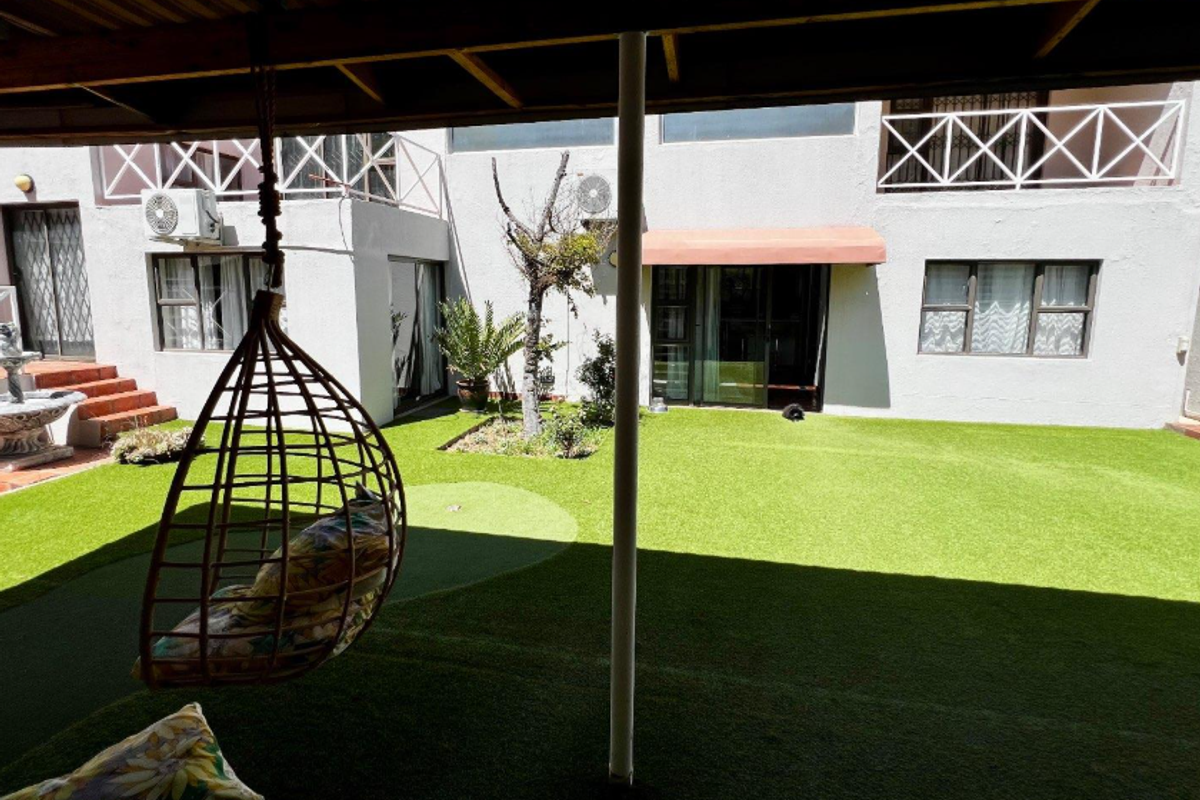 A private rear courtyard featuring a covered patio, artificial lawn, and access to the main dwelling via sliding doors and a balcony above.