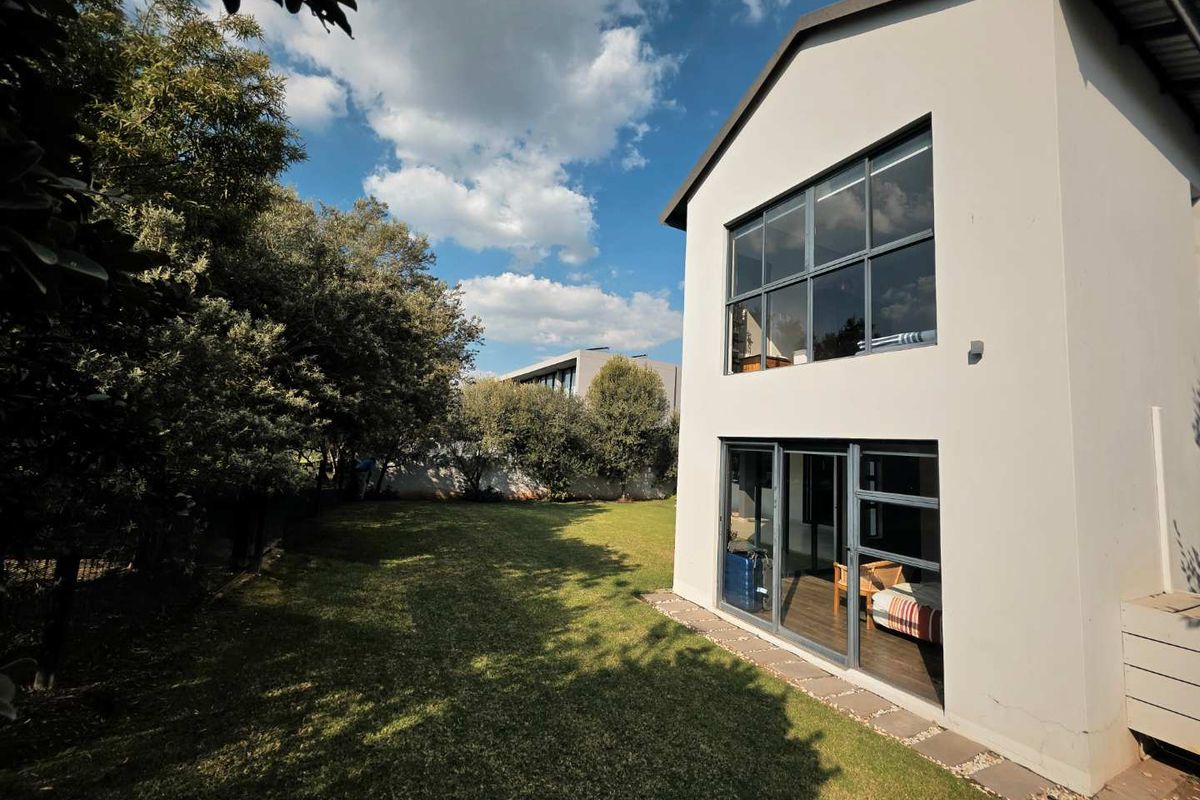 A view of the rear exterior of the house, featuring a two-story facade with large windows, sliding glass doors, and a well-maintained garden.