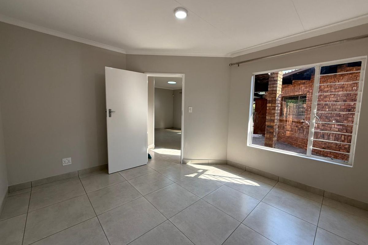 A bright, empty bedroom featuring neutral wall tones, large windows with security bars, and tiled flooring, offering a clean and versatile living space.