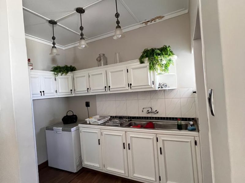 A functional scullery area featuring built-in white cabinetry, a stainless steel sink, and tiled backsplash, requiring minor ceiling repairs.