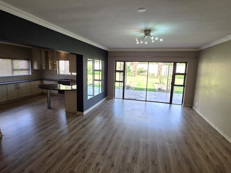 Spacious open-plan living area featuring laminate flooring, modern kitchen cabinetry, and large sliding glass doors providing direct access to the rear garden.