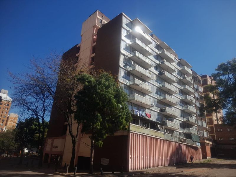 A multi-story apartment building featuring a series of private balconies and a prominent concrete facade under a clear blue sky.