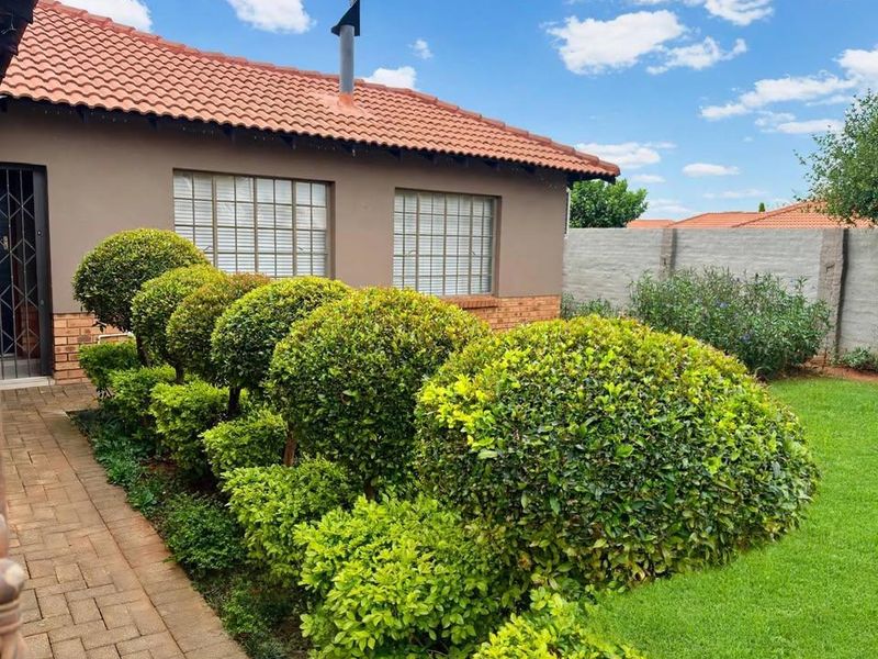 Rear view of the house featuring a terracotta tiled roof, brick exterior, paved walkway, and a well-maintained garden with manicured shrubs.
