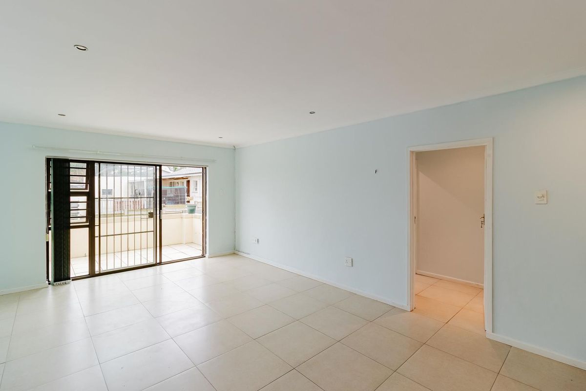 A bright, empty living room featuring neutral floor tiles, recessed ceiling lighting, and sliding glass doors leading to an outdoor balcony area.