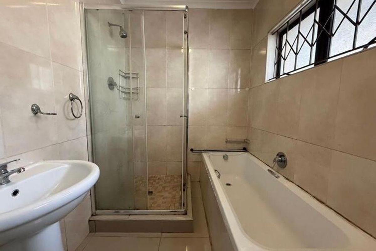 A functional bathroom featuring a separate shower enclosure, bathtub, and pedestal basin with neutral wall and floor tiling.
