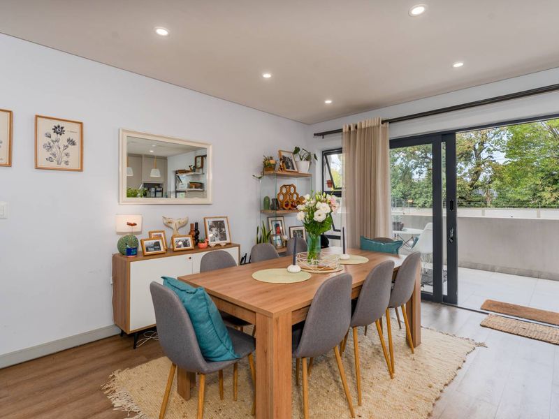 Bright dining area featuring modern laminate flooring, recessed downlighting, and seamless access to an outdoor balcony through large sliding glass doors.