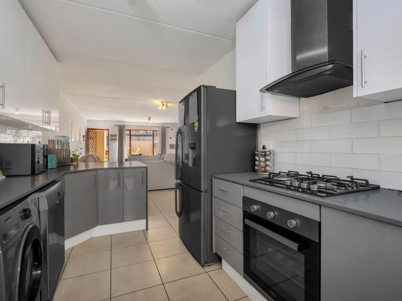 Modern open-plan kitchen featuring grey cabinetry, stone countertops, subway tile backsplash, and integrated gas hob with extractor fan, flowing into the living area.