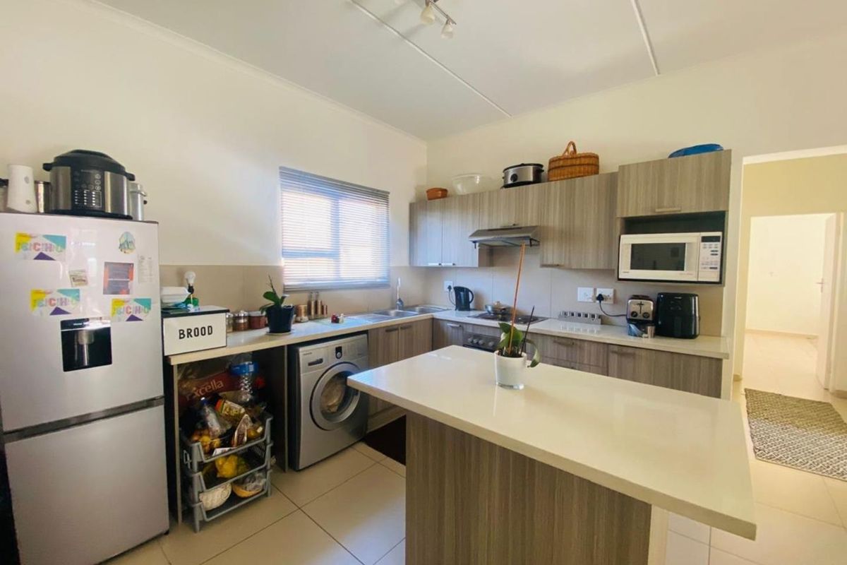 Functional kitchen featuring wood-look cabinetry, stone-style countertops, integrated laundry plumbing, and a central island, providing a practical workspace for daily meal preparation.
