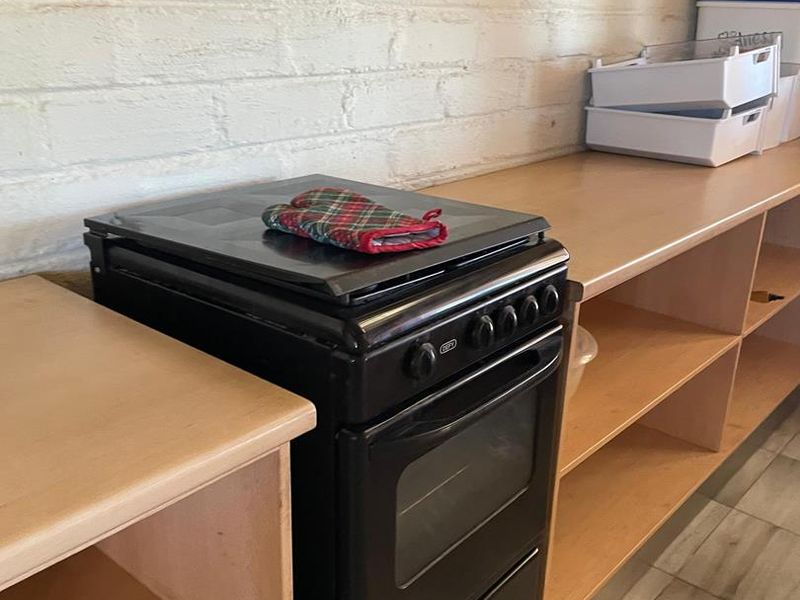 A functional kitchen area featuring a freestanding stove, open wooden shelving units, and tiled flooring against a painted brick wall.