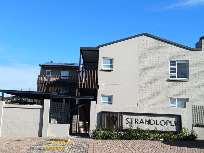 Front elevation of the Strandloper apartment complex featuring a modern brick facade, secure gated entrance, paved driveway, and balconies with timber-style screening.
