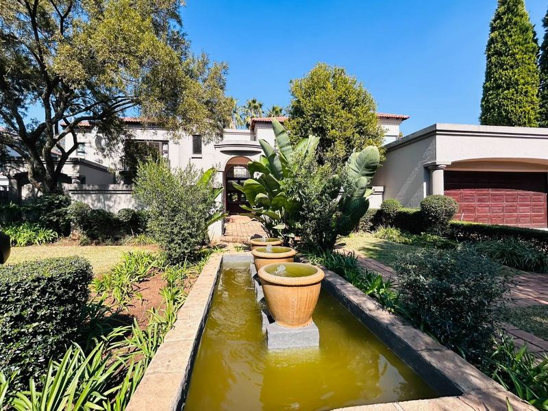 Front elevation of a house featuring a landscaped garden, a paved driveway, a garage, and a decorative water feature.