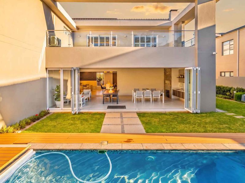 Rear view of a modern home featuring a swimming pool, timber deck, covered patio with built-in braai, and seamless indoor-outdoor flow through bi-fold doors.