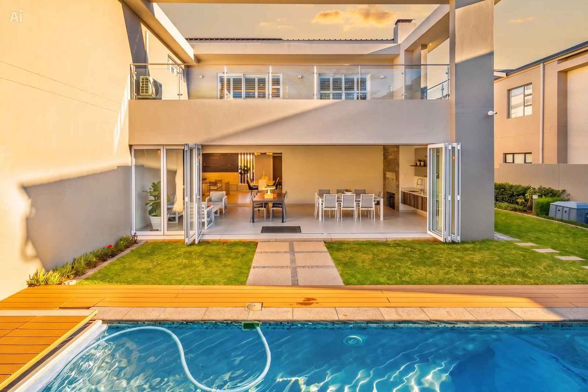 Rear view of a modern home featuring a swimming pool, timber deck, covered patio with built-in braai, and seamless indoor-outdoor flow through bi-fold doors.