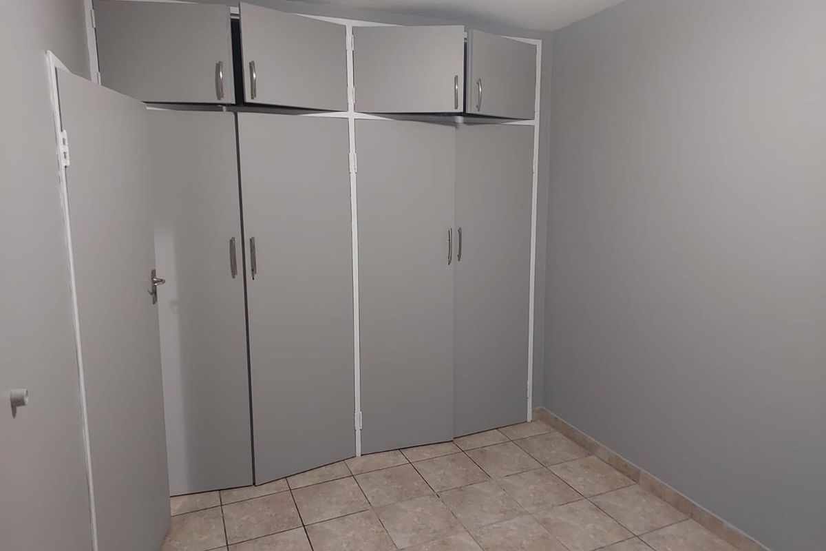 A bedroom featuring built-in floor-to-ceiling cabinetry with overhead storage and neutral tiled flooring.