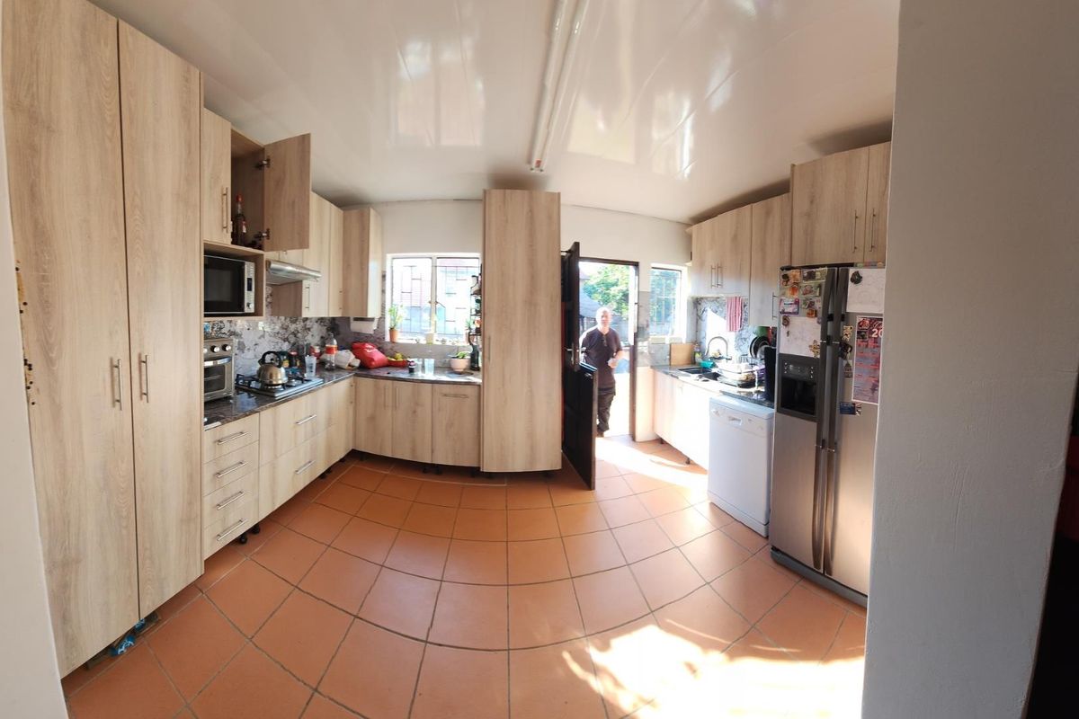 A functional kitchen featuring light wood-look cabinetry, tiled flooring, and integrated appliances, offering a practical layout with direct access to the exterior.
