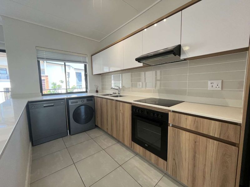 Modern kitchen featuring sleek white and wood-grain cabinetry, stone countertops, tiled backsplash, and integrated appliances including an oven, cooktop, and extractor fan.