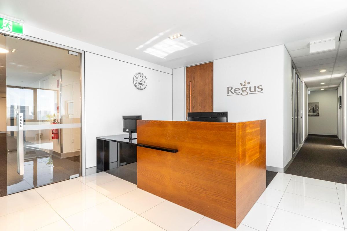 Professional office reception area featuring a built-in wooden desk, glass entry door, and clean tiled flooring in a modern corporate environment.
