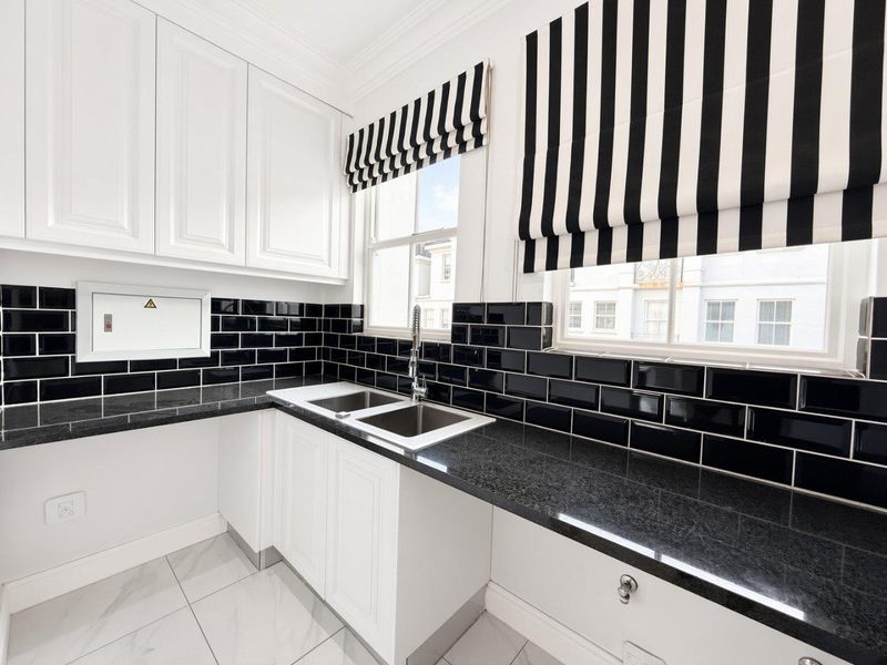 A clean and modern scullery featuring white cabinetry, black granite countertops, a double sink, and a striking black subway tile backsplash.