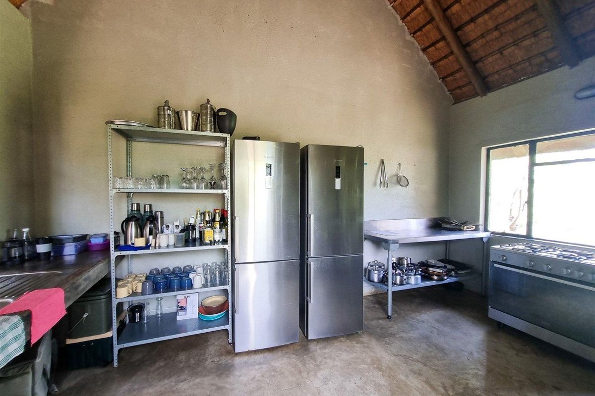 A rustic kitchen area featuring a high thatched ceiling, concrete flooring, stainless steel prep tables, and a freestanding gas stove.